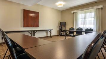 Une salle de conférence avec une longue table, des chaises, un téléviseur et une fenêtre avec des rideaux.