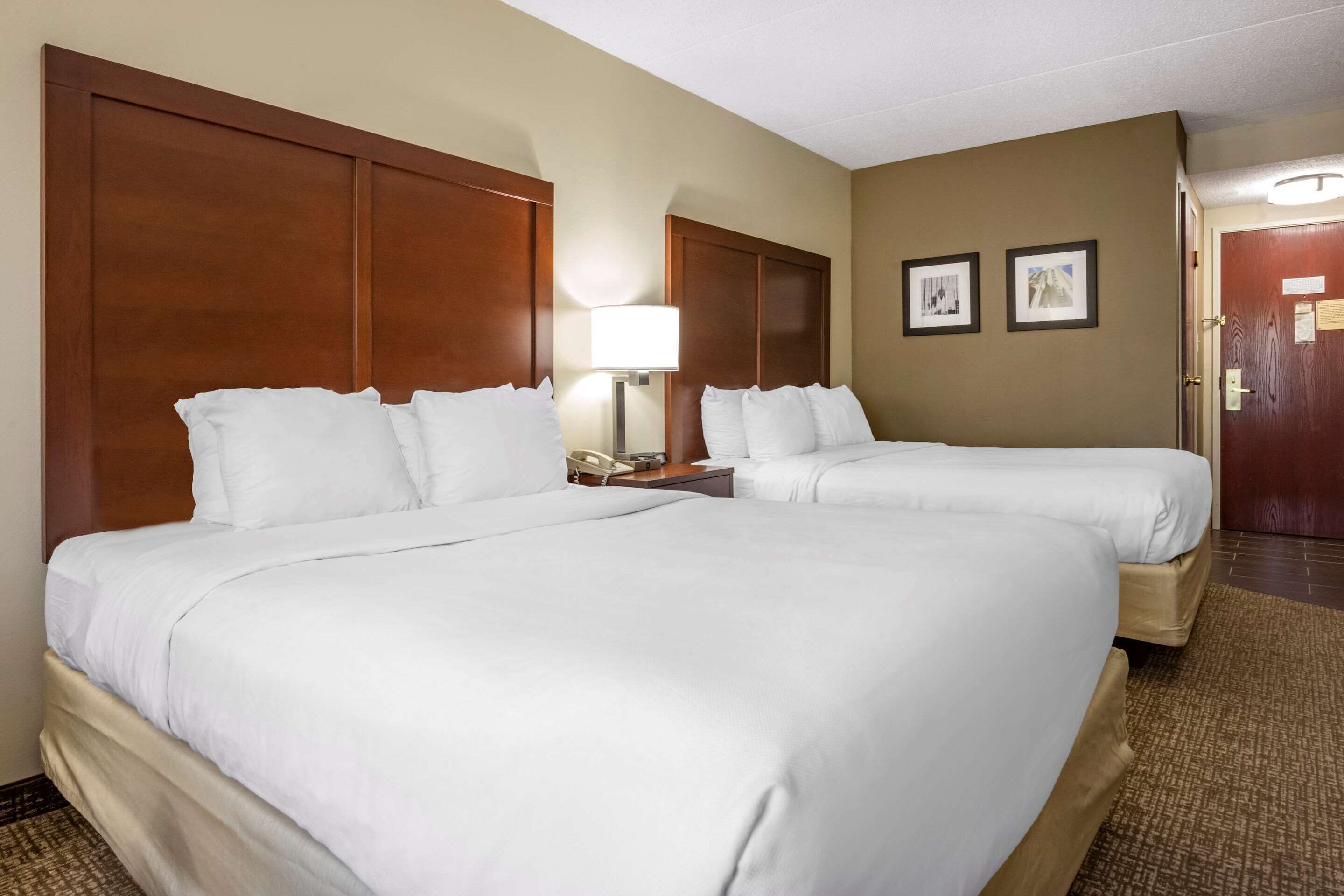 A hotel room with two beds, a nightstand with a lamp, and a door with a plaque.