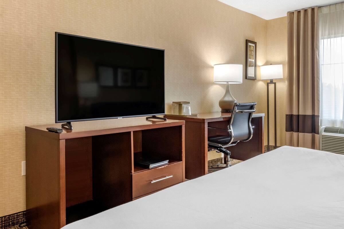 Une chambre d’hôtel équipée d’un grand téléviseur à écran plat, d’un bureau avec une chaise, d’une lampe et d’un lit.