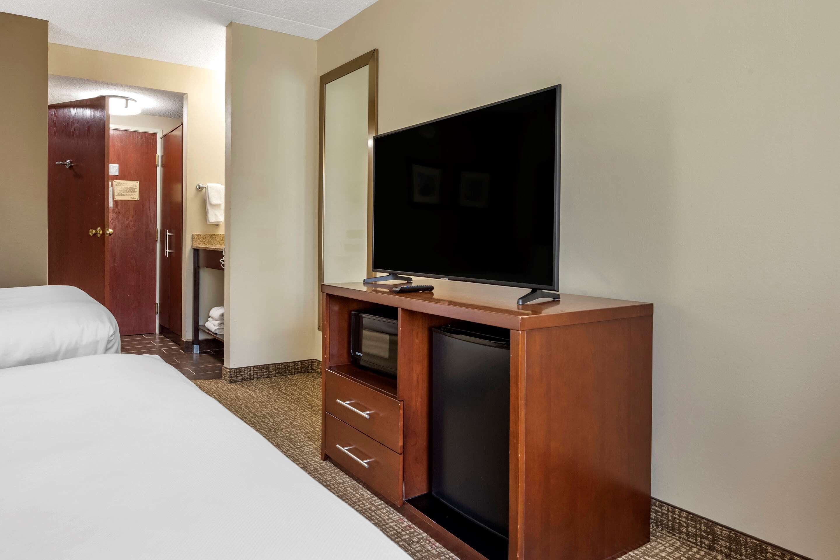 A hotel room with two beds, a TV on a wooden stand, a small desk with drawers, and a bathroom visible through an open door.