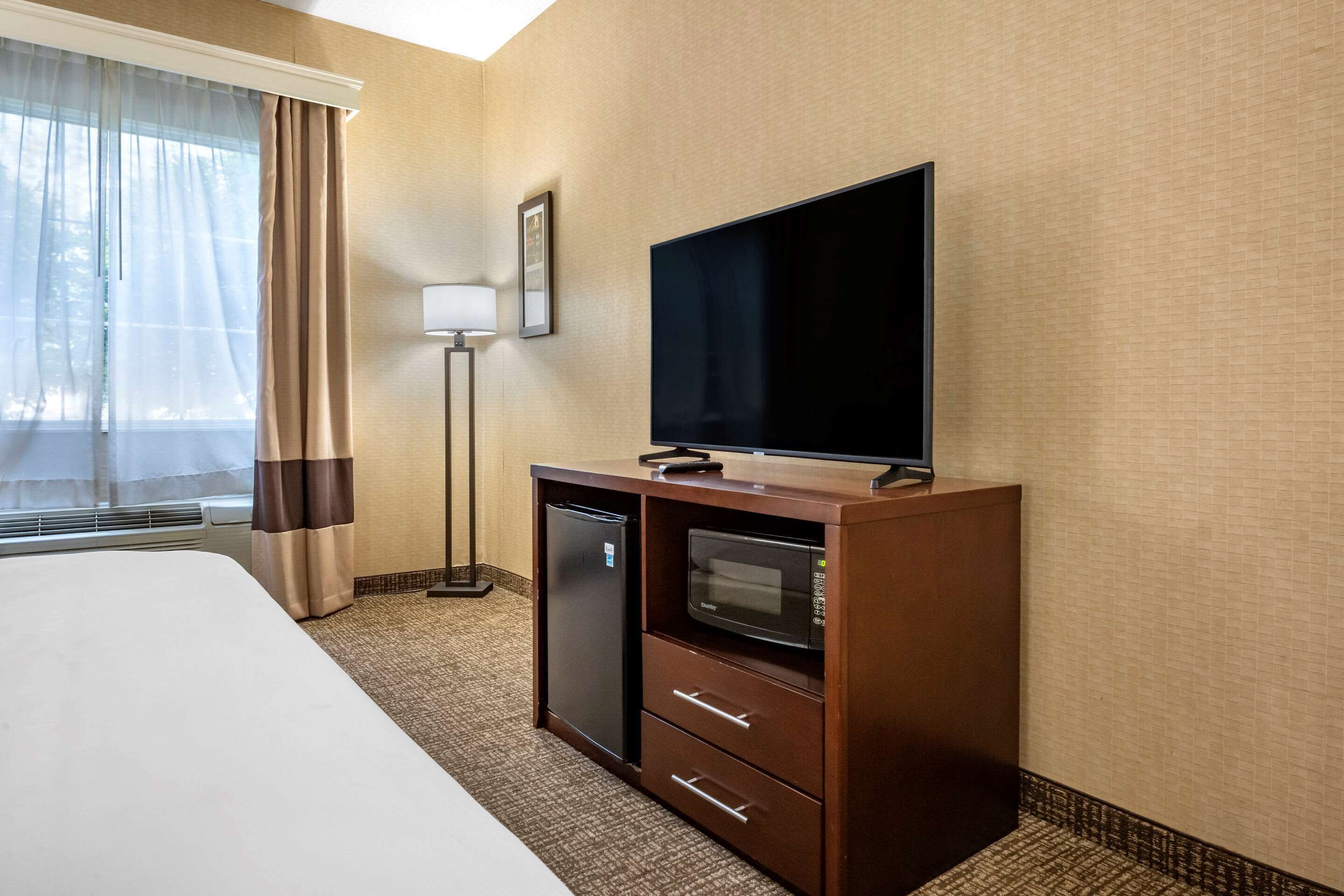 A hotel room with a bed, a flat-screen TV, a mini-fridge, a microwave, and a desk with drawers.