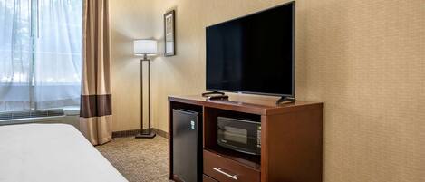 A hotel room with a bed, a flat-screen TV, a mini-fridge, a microwave, and a desk with drawers.