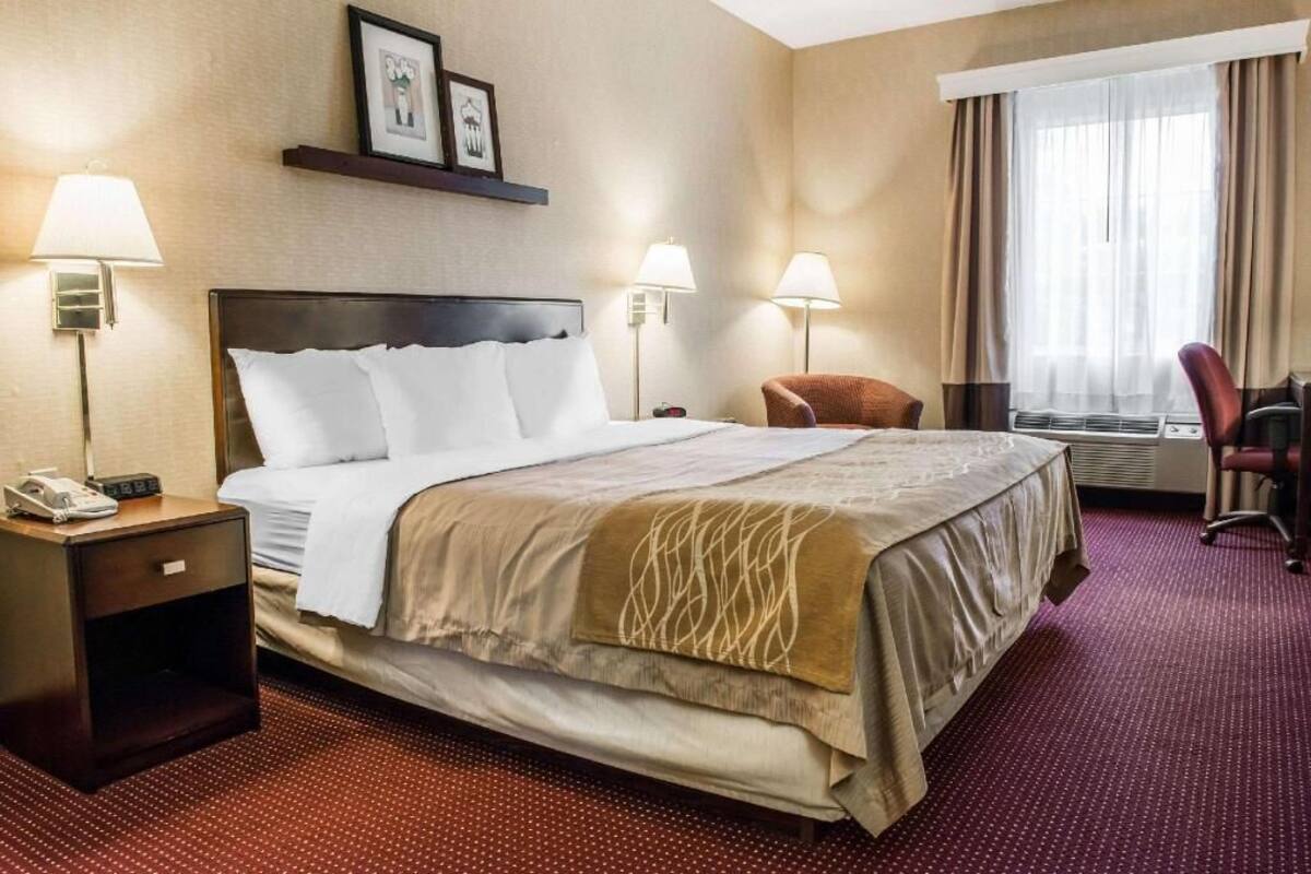 Une chambre d’hôtel avec un lit, deux lampes de chevet, une chaise, un bureau avec un téléphone et une fenêtre avec des rideaux.