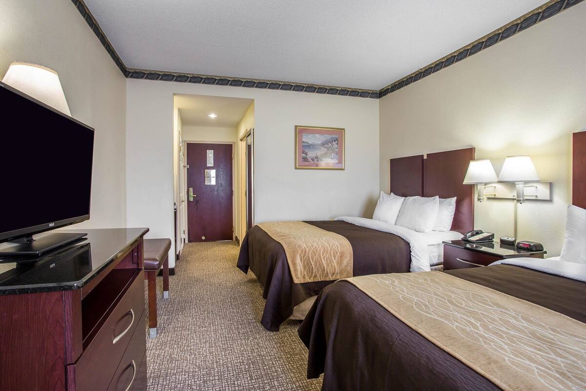 A hotel room with two beds, a desk with a television, and a door leading to another room.