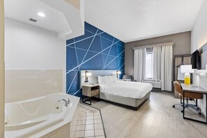 A hotel room with a large bed, a desk, a chair, a desk lamp, a TV, a bathroom with a bathtub, and a window with curtains. - Comfort Inn & Suites Ft. Jackson Maingate (Columbia)