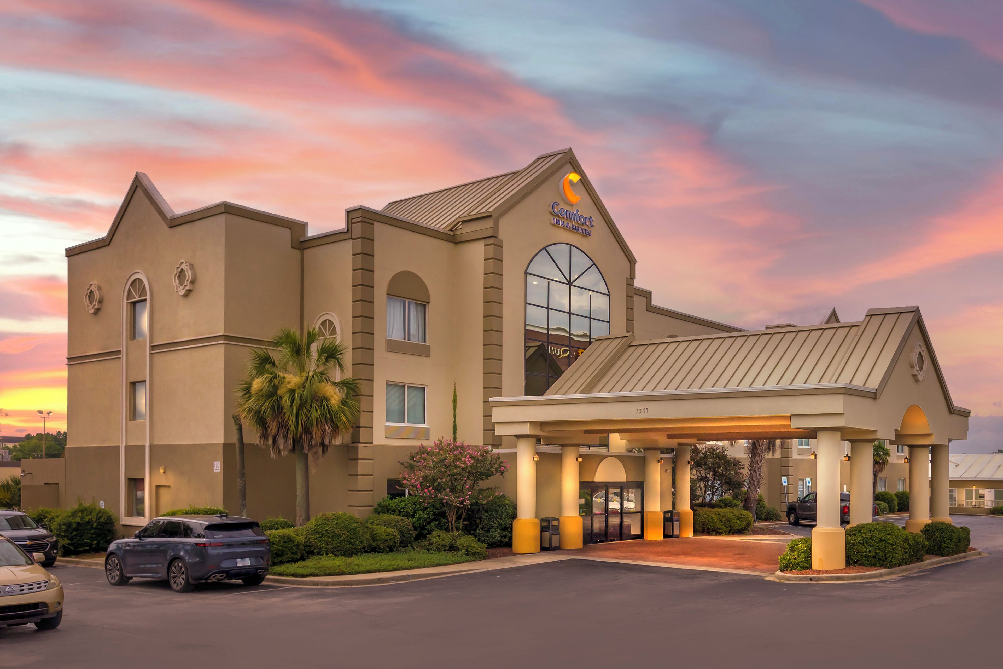 A hotel with a large arched entrance, a prominent 'Comfort Inn & Suites' sign, and a parking lot with several cars.