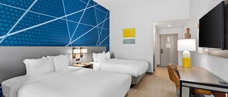 A hotel room with two beds, a desk, a chair, a TV, and a modern wall design.