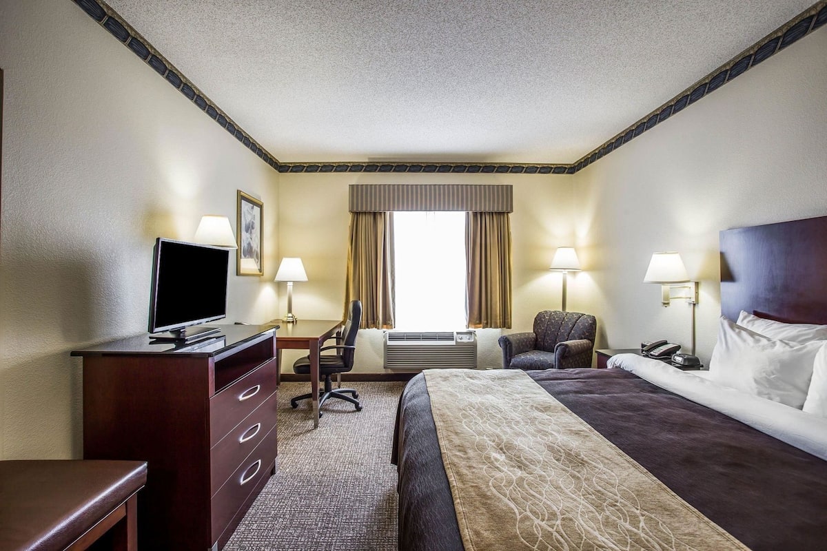 A hotel room with a bed, desk, chair, TV, and lamps.