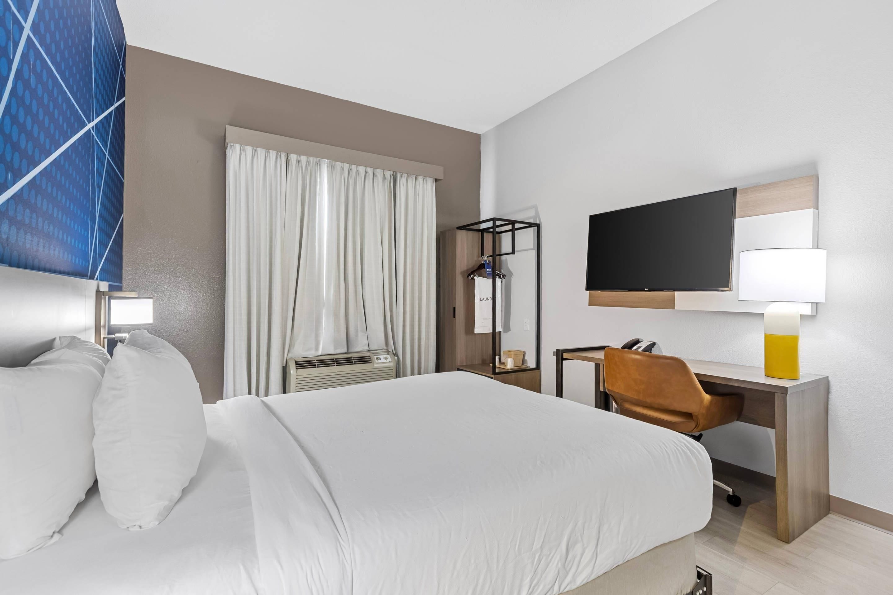 Een hotelkamer met een bed, een bureau, een stoel, een televisie en een raam met gordijnen.