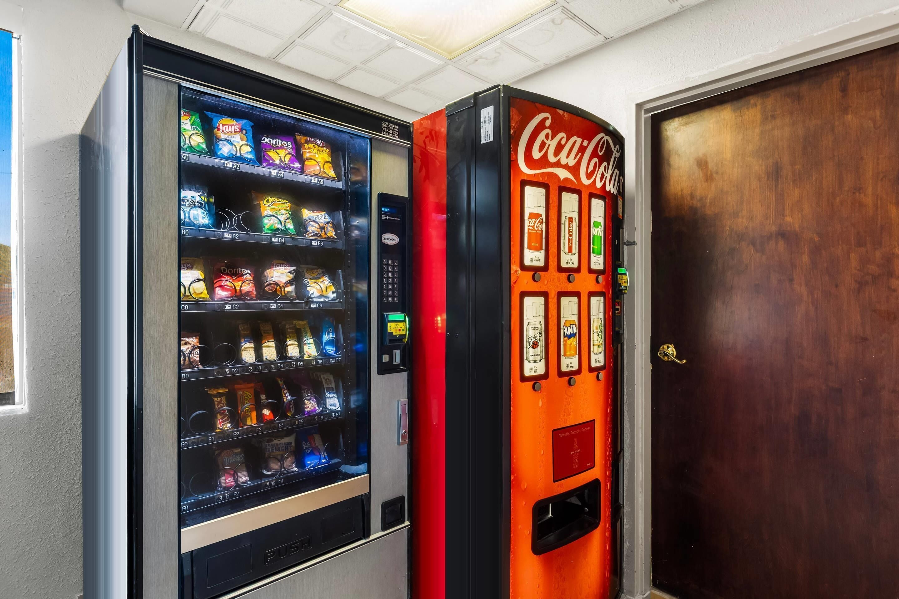 Máquina de vendas com lanches e Coca-Cola, ao lado de uma porta de madeira.