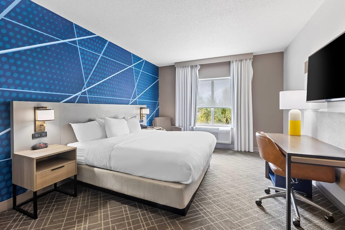 A hotel room with a bed, bedside table, lamp, desk, chair, and a TV.