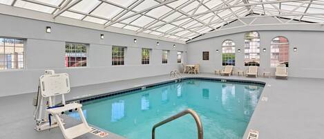 An indoor swimming pool with a glass ceiling, poolside chairs, and a lifeguard chair.