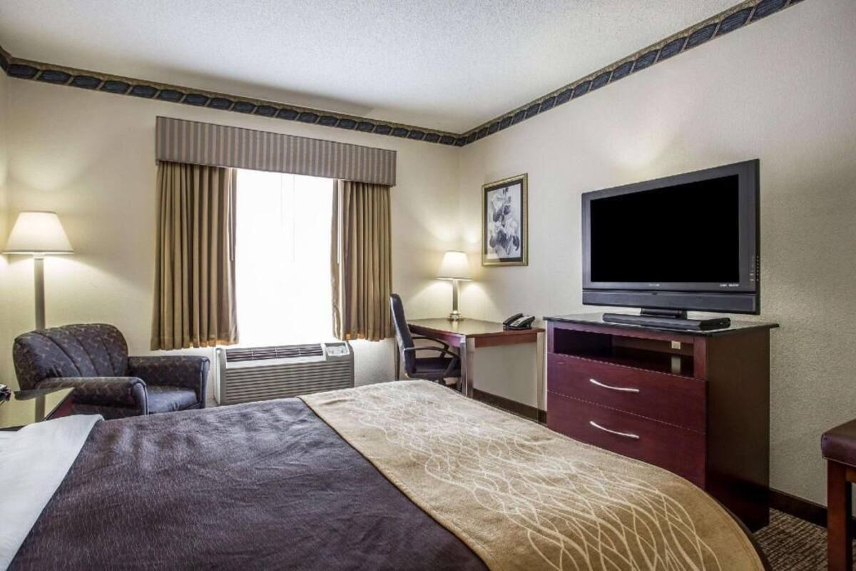 A hotel room with a bed, desk, chair, television, and a window with curtains.