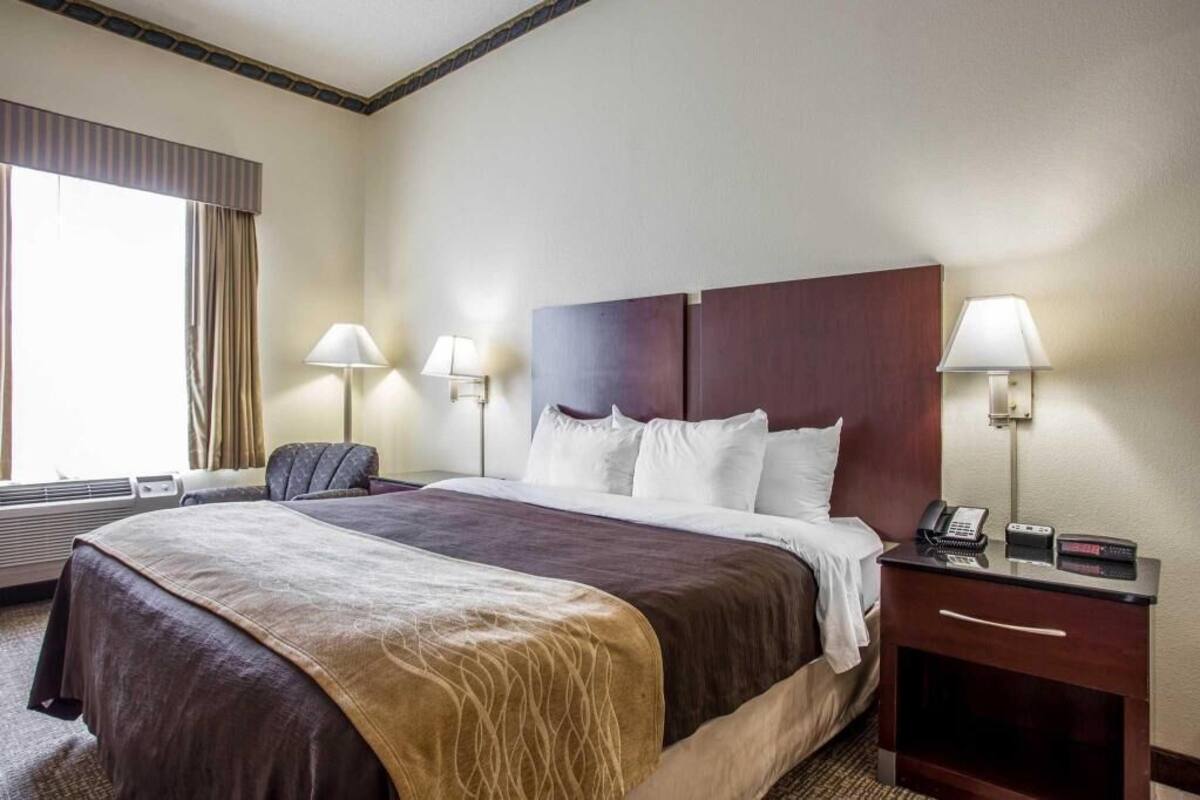 A hotel room with a large bed, two bedside lamps, a desk with a phone, and a window with curtains.