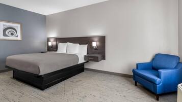 Habitación de hotel con una cama, una mesita de noche, una silla azul y una lámpara de pared.