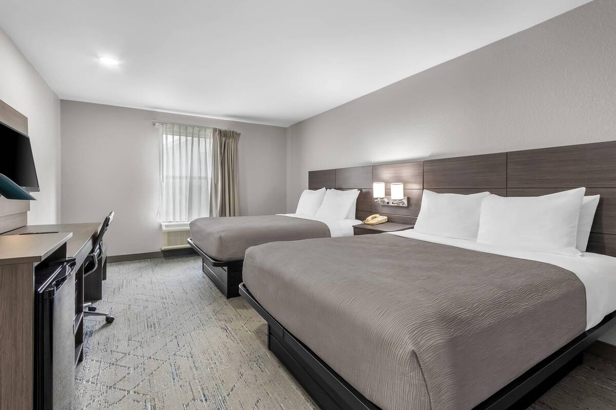 A hotel room with a bed, bedside table, lamp, desk, chair, and a TV.