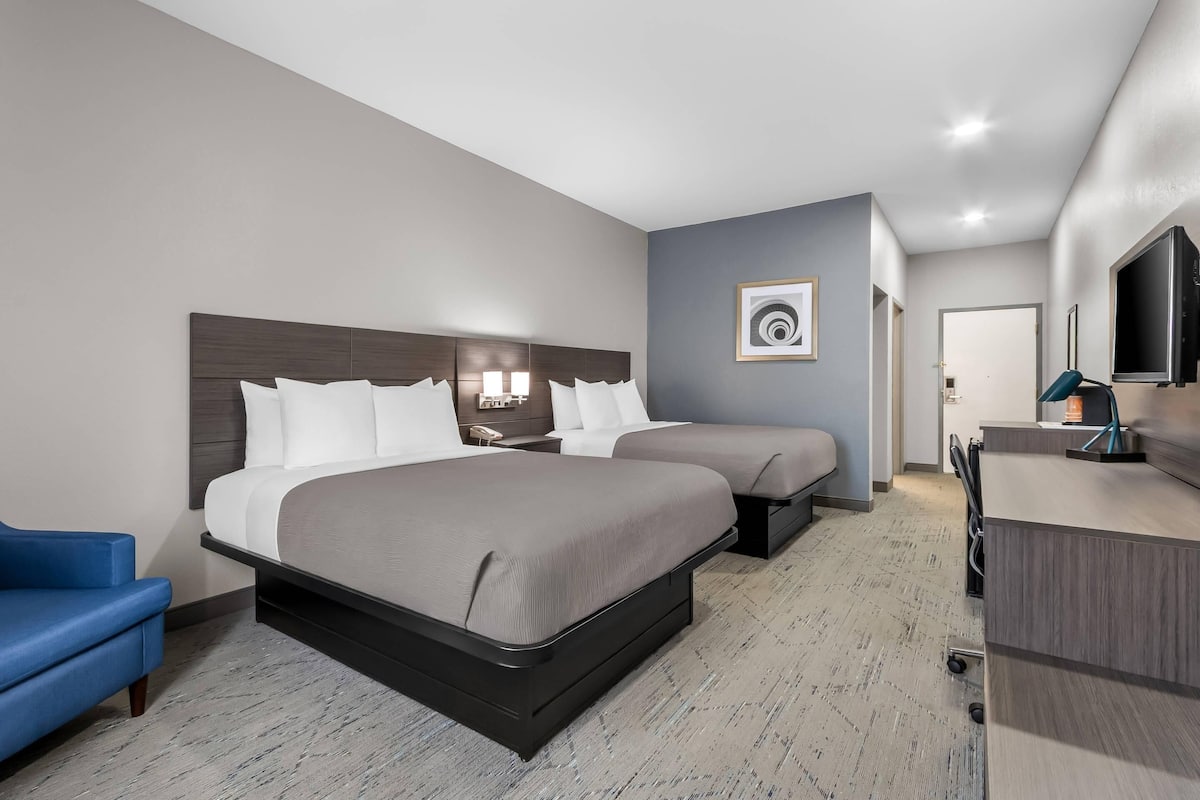 A hotel room with two beds, a desk, a chair, and a television.