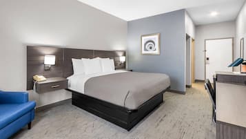 A hotel room with a bed, bedside table, lamp, and a desk with a chair.