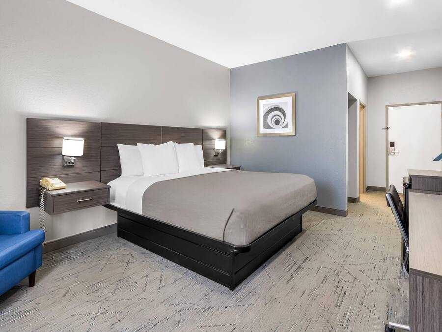 A hotel room with a bed, bedside table, lamp, and a desk with a chair.