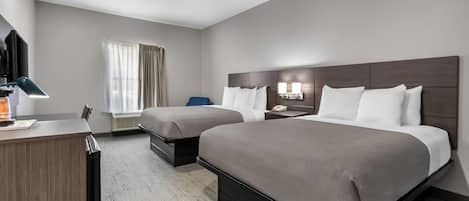 Une chambre d’hôtel avec deux lits, un bureau, une télévision et une fenêtre avec des rideaux.