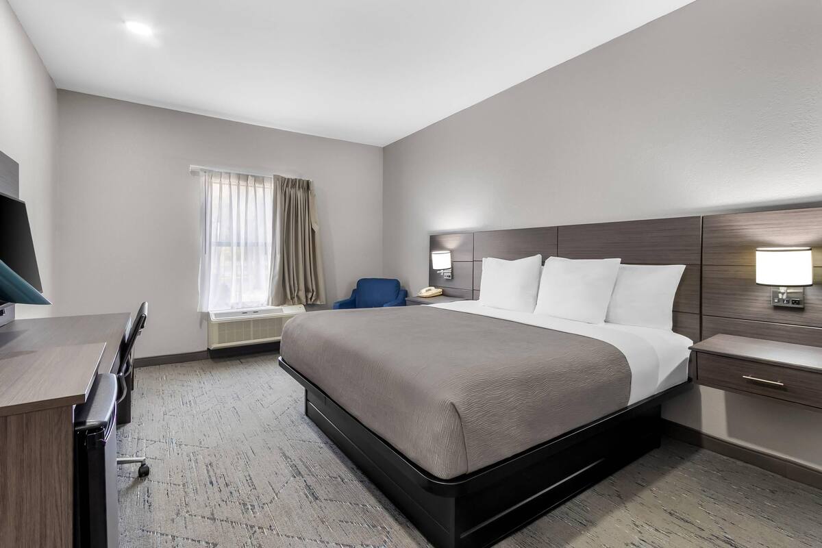 A hotel room with a bed, desk, chair, and bedside lamps.