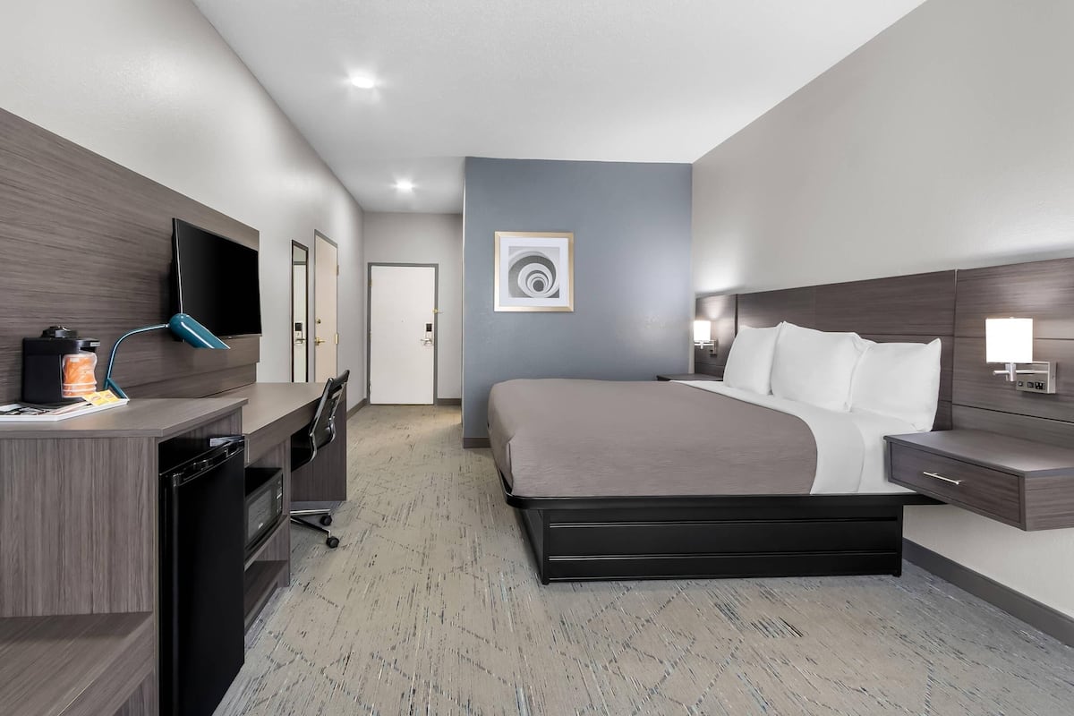 A modern hotel room with a bed, desk, and TV.