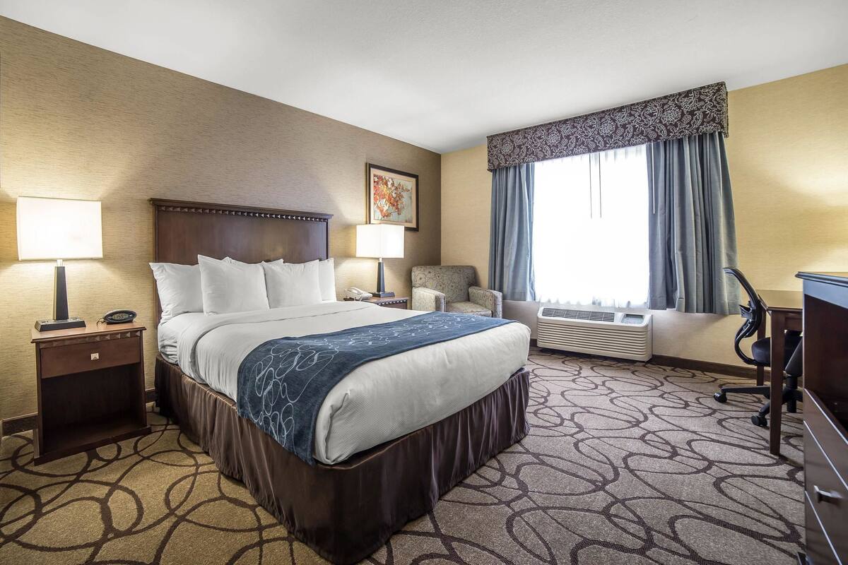 A hotel room with a large bed, two bedside tables with lamps, a chair, a desk, and a window with curtains.