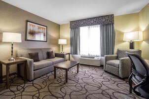 Habitación de hotel con sofá, sillón y una pequeña mesa. Se observa una ventana con cortinas y un equipo de aire acondicionado.