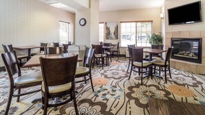 Une salle à manger d’hôtel avec plusieurs tables et chaises, une horloge au mur et un téléviseur à écran plat fixé au-dessus d’une cheminée.
