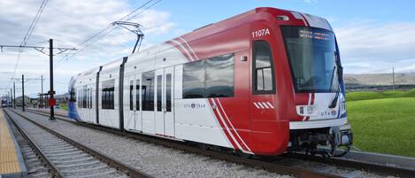 Un tren rojo y blanco con el número 1107A en la parte frontal, circulando sobre rieles con líneas de suministro eléctrico aéreas.