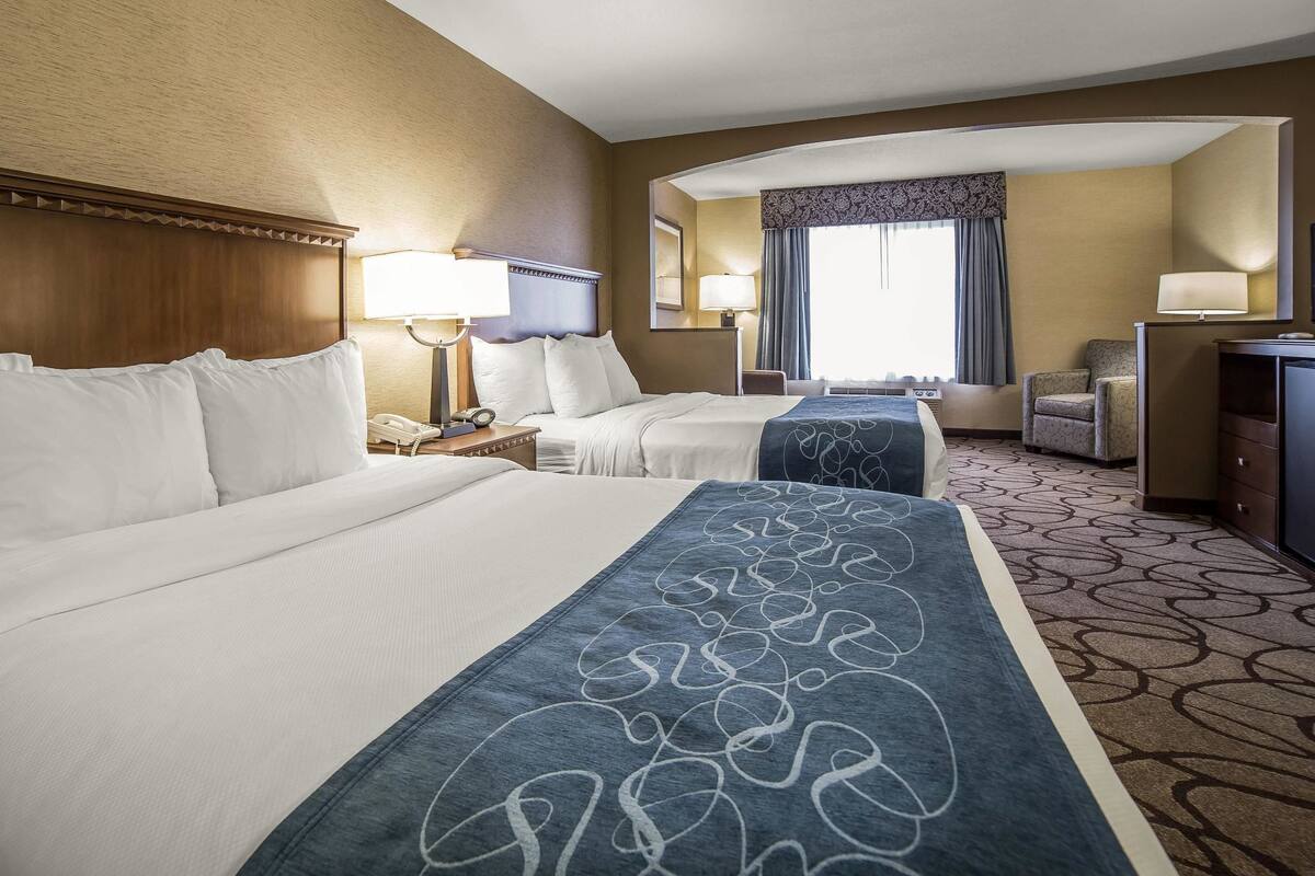 A hotel room with two beds, a desk, a chair, and a large window with curtains.
