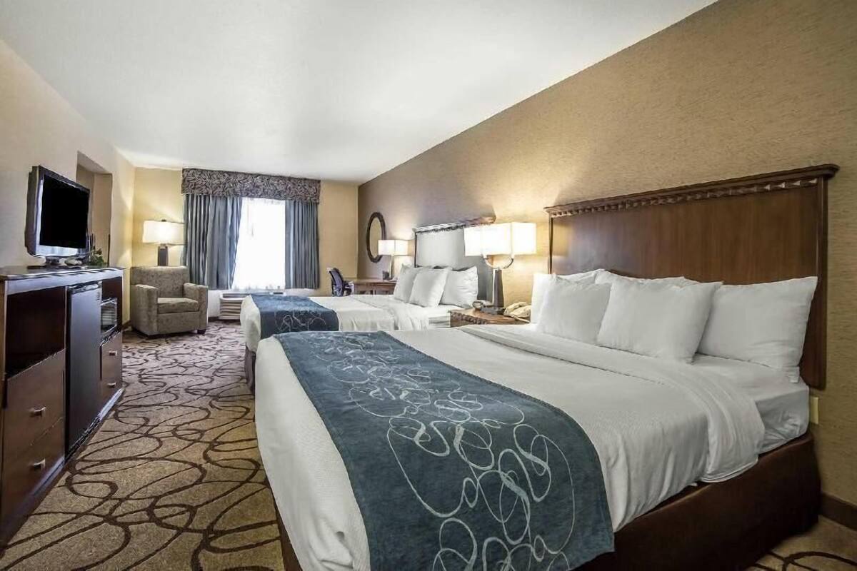 A hotel room with two beds, a desk, a television, and a chair.