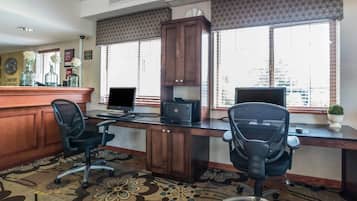 A hotel office with two desks, two chairs, a printer, and a computer monitor.