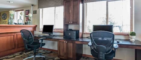 A hotel office with two desks, two chairs, a printer, and a computer monitor.