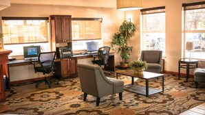 Un hall d’hôtel comprenant un bureau avec ordinateur, deux chaises, une table basse, une plante en pot et un tapis à motifs.