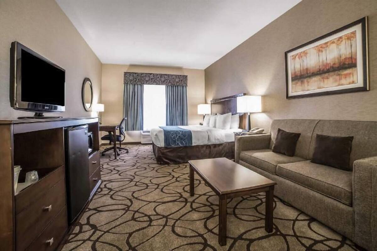 A hotel room with a bed, a sofa, a TV, a desk, and a large painting on the wall.