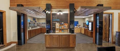 Un café avec un comptoir central, des meubles en bois et une enseigne sur laquelle on peut lire : « IL FAUT ABSOLUMENT PRENDRE UN CAFÉ ».