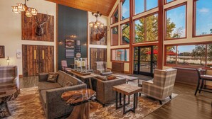 A spacious lobby with a large window overlooking a lake, furnished with leather sofas and wooden tables, and featuring rustic decor including antler wall art. - Holiday Inn Express & Suites Hayward by IHG (Hayward)