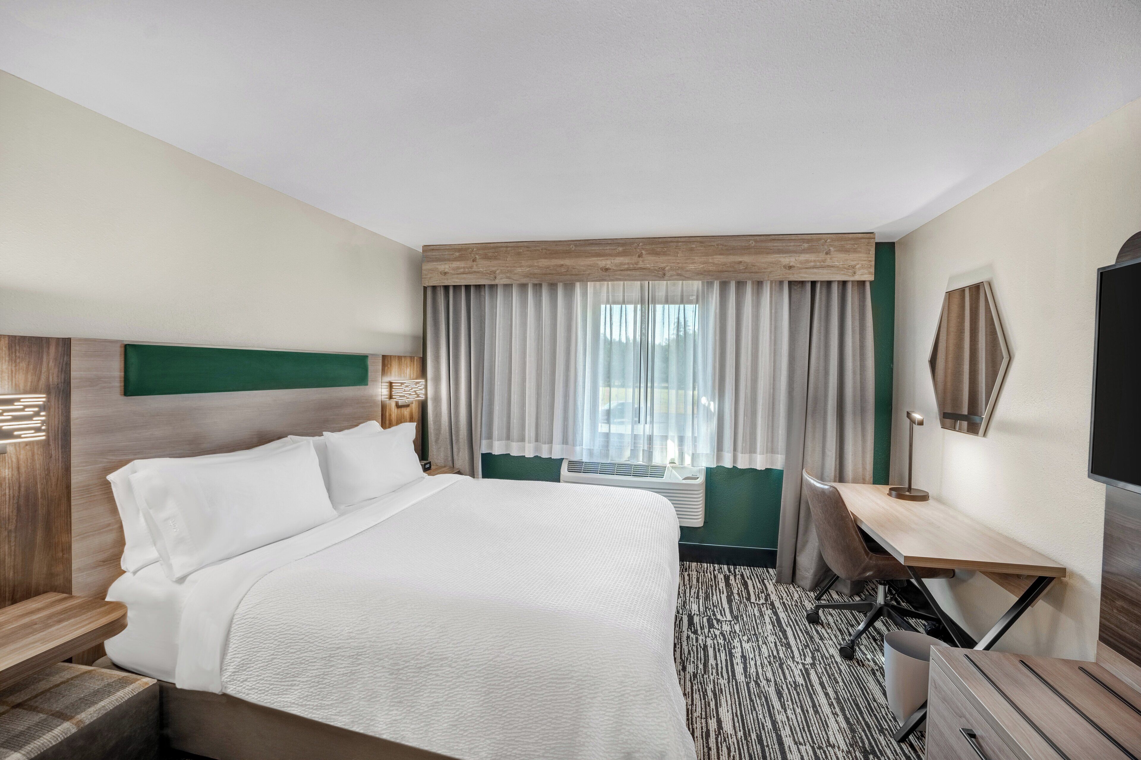 Een hotelkamer met een groot bed, een bureau, een stoel, een televisie en een raam met gordijnen.