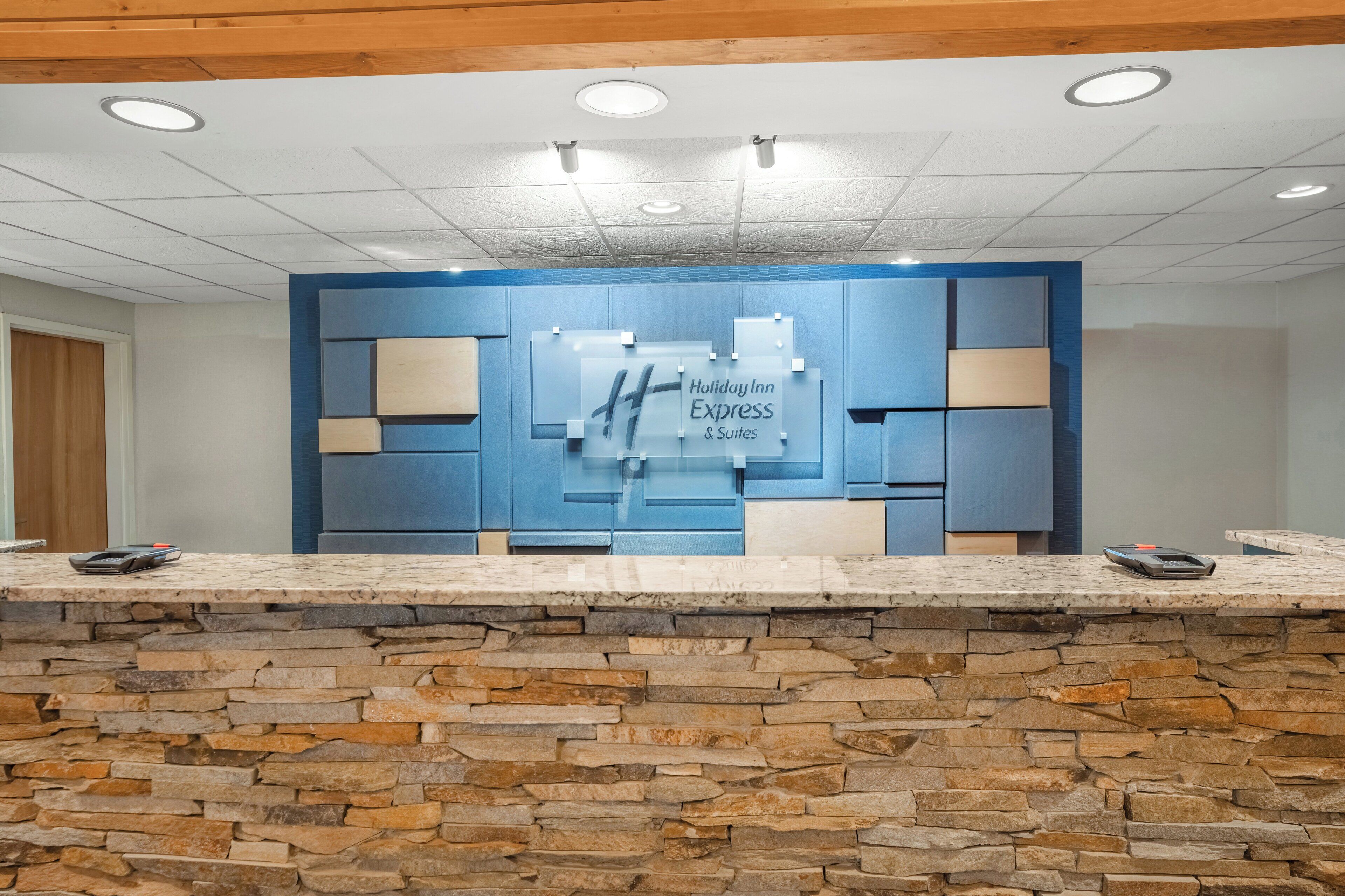A reception desk with a stone wall base, a blue panel wall, and a sign reading "Holiday Inn Express & Suites".