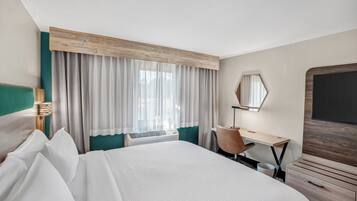 A hotel room with a large bed, a desk, a chair, a TV, and a window with curtains.