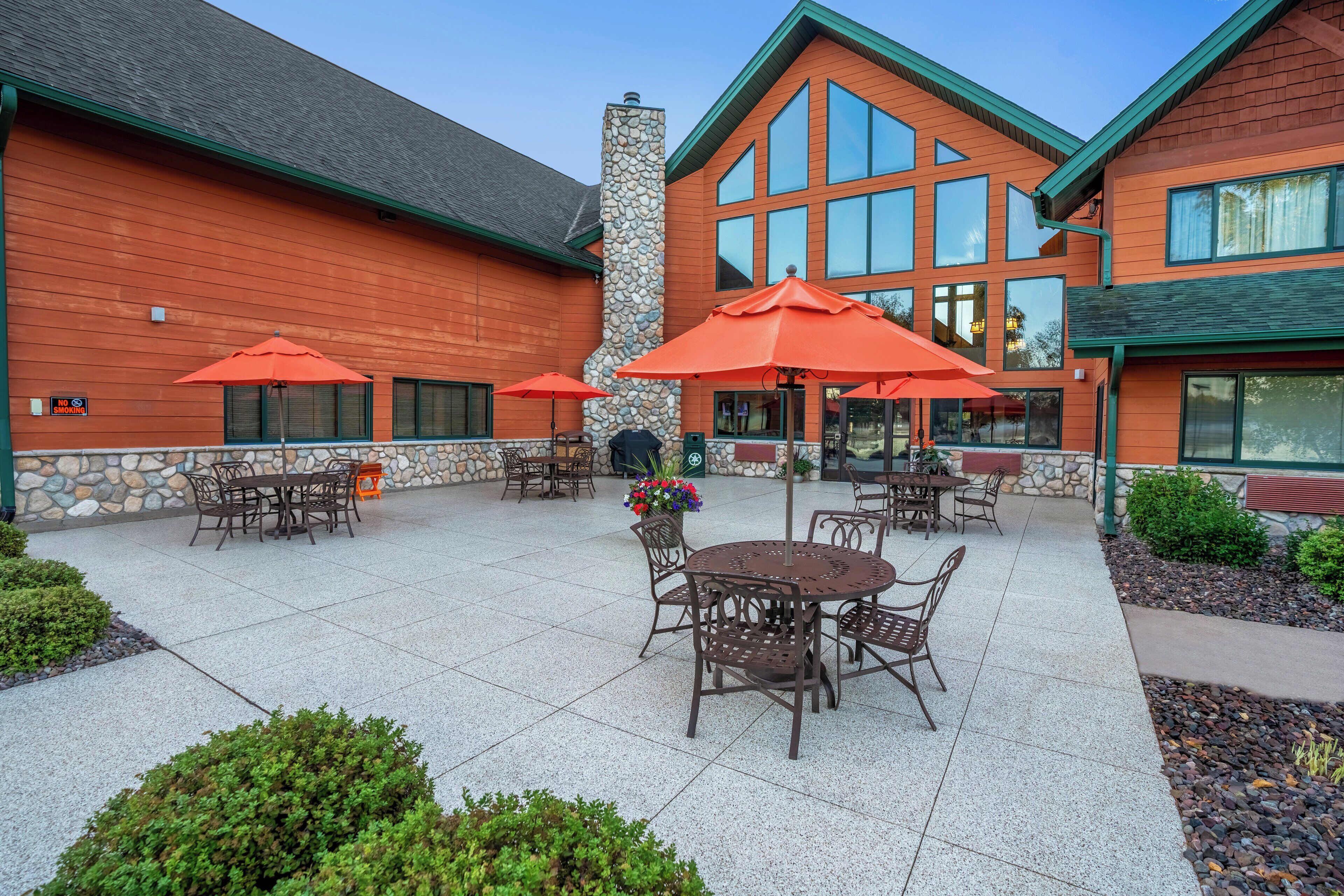 An outdoor patio with tables and chairs, stone walls, and a brick building with large windows.