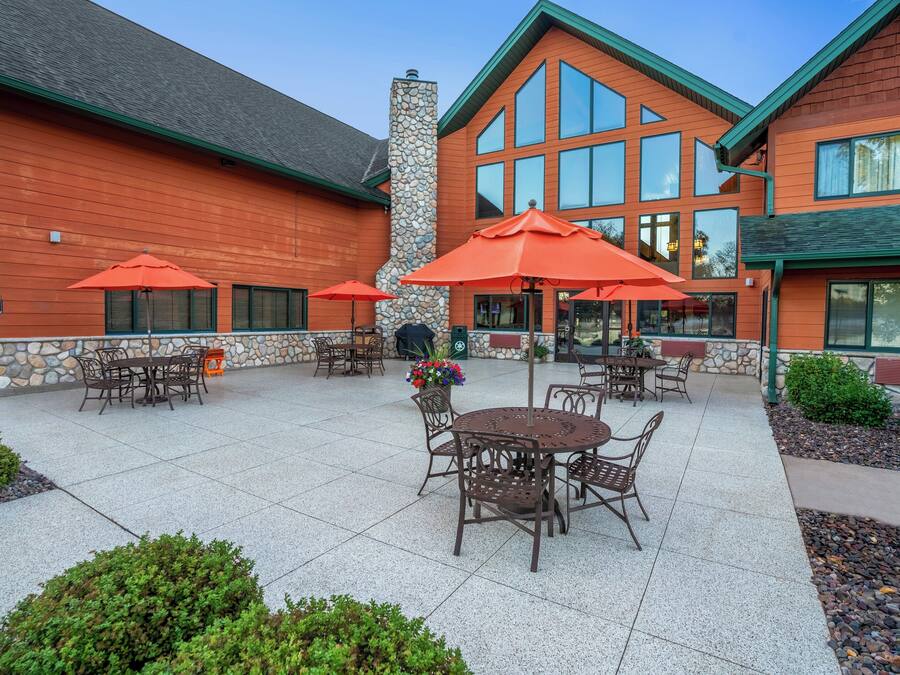 An outdoor patio with tables and chairs, stone walls, and a brick building with large windows.