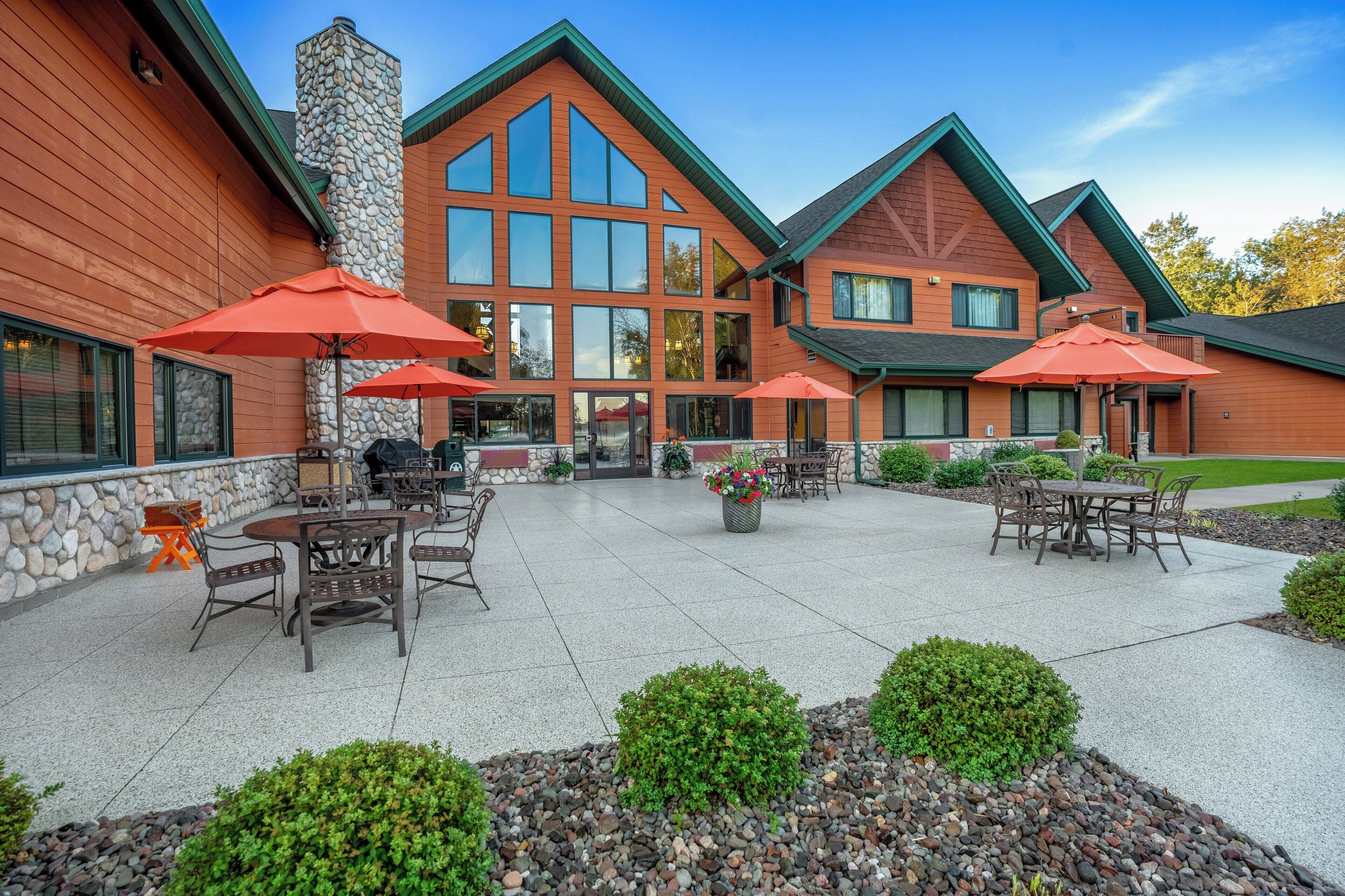 A building with a stone chimney, large windows, and outdoor seating with umbrellas.
