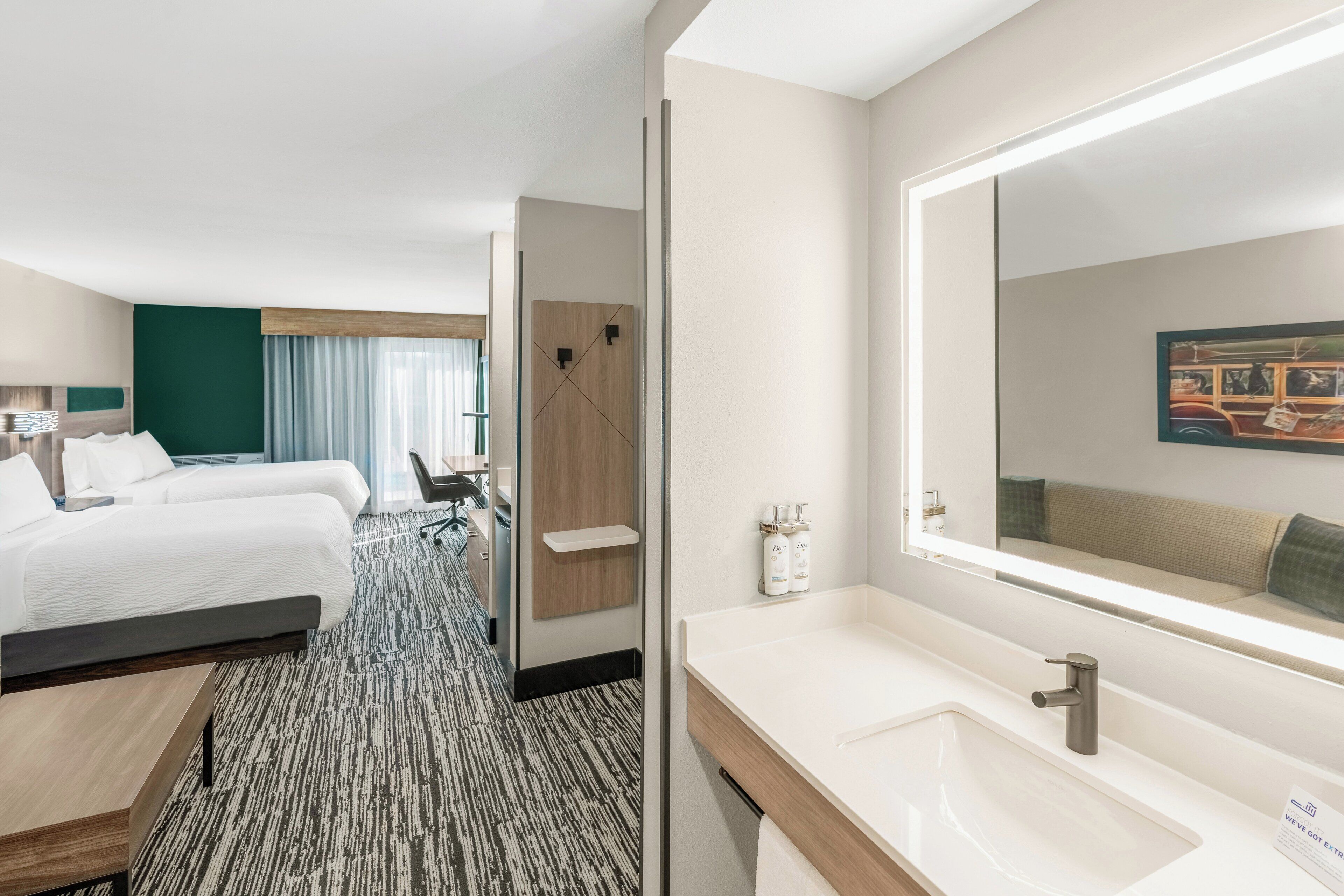 A hotel room with two beds, a large mirror, a sink, and a shower area.