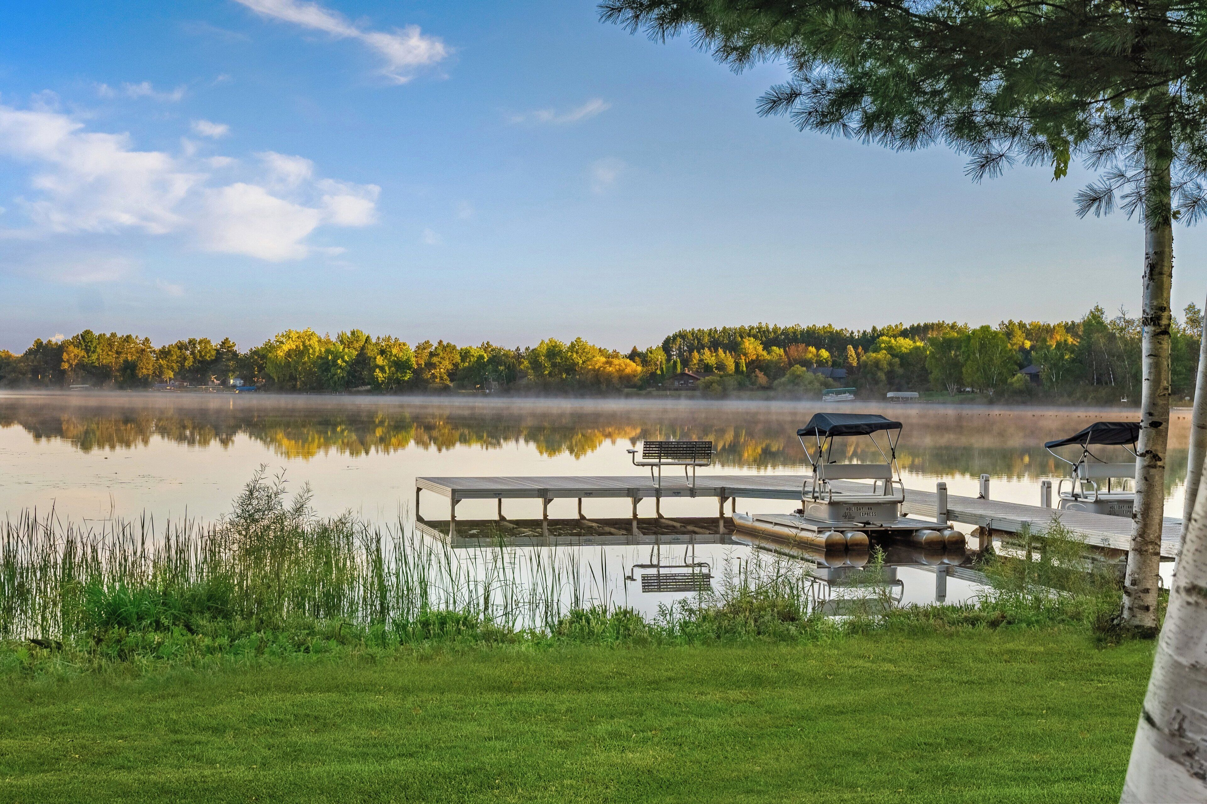 Une vue sur le lac, avec un quai, des bancs et une rangée d’arbres en arrière-plan.
