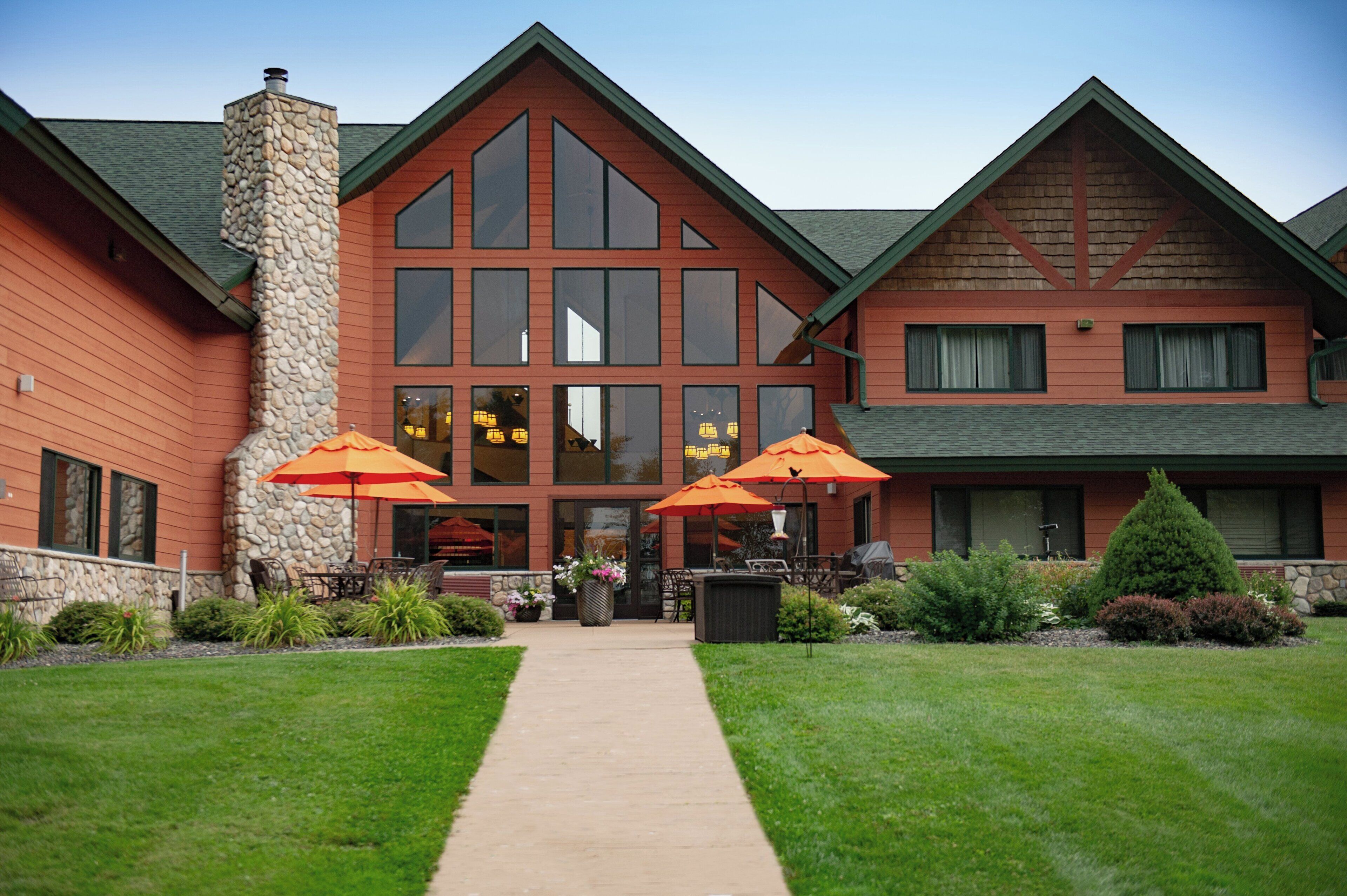 A two-story building with a stone chimney, large windows, and outdoor umbrellas.