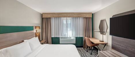 A hotel room with a large bed, a desk, a chair, a flat-screen TV, and a window with curtains.