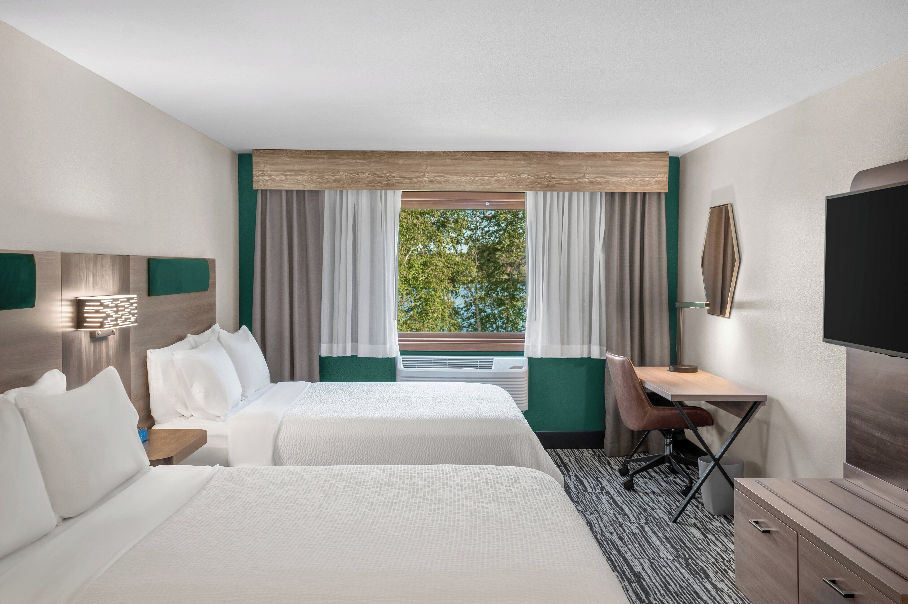 Een hotelkamer met twee bedden, een bureau, een stoel, een televisie en een raam met gordijnen.