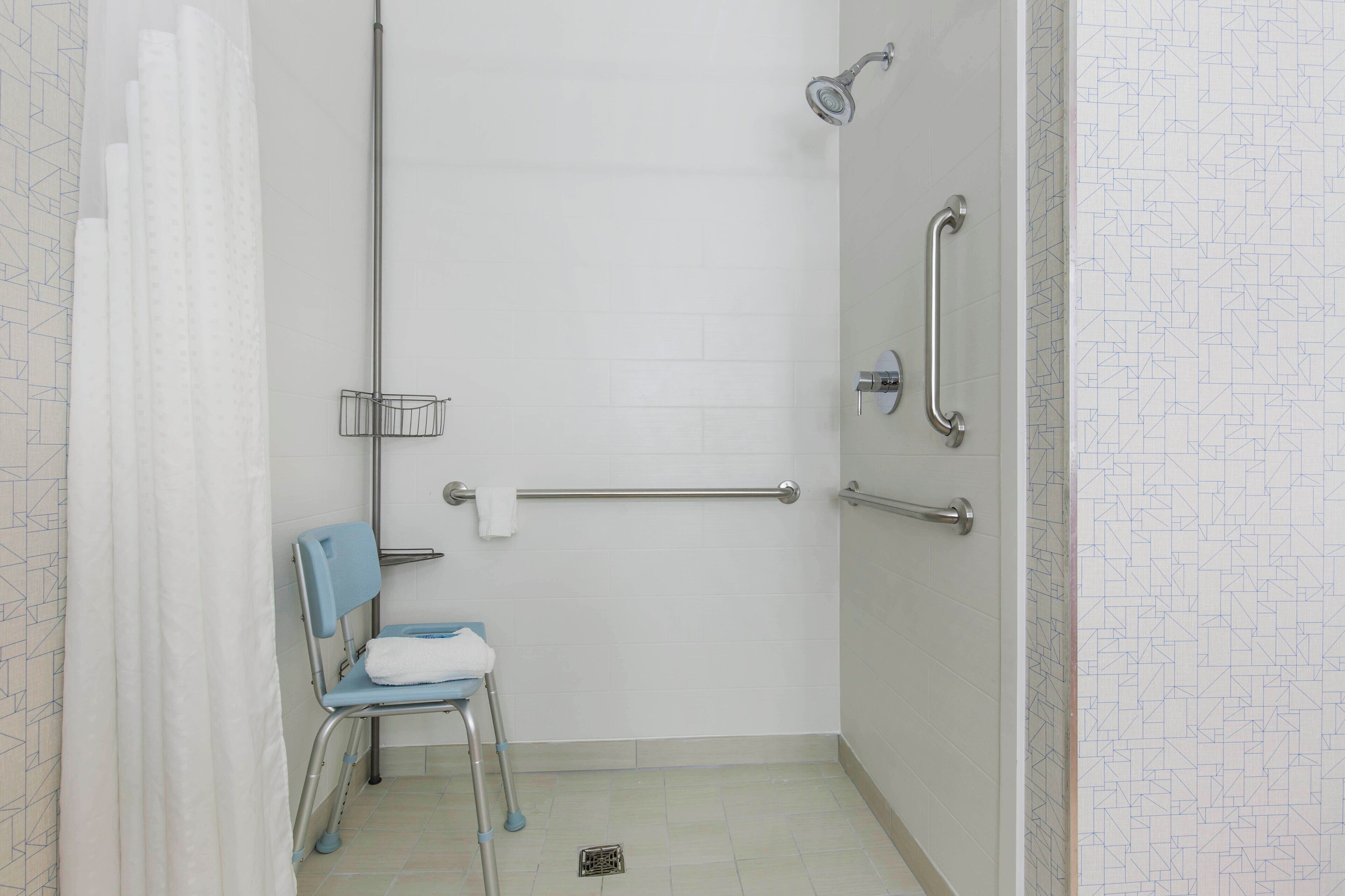 Cabina doccia accessibile in sedia a rotelle, dotata di maniglie di sostegno, porta asciugamani e sedile.